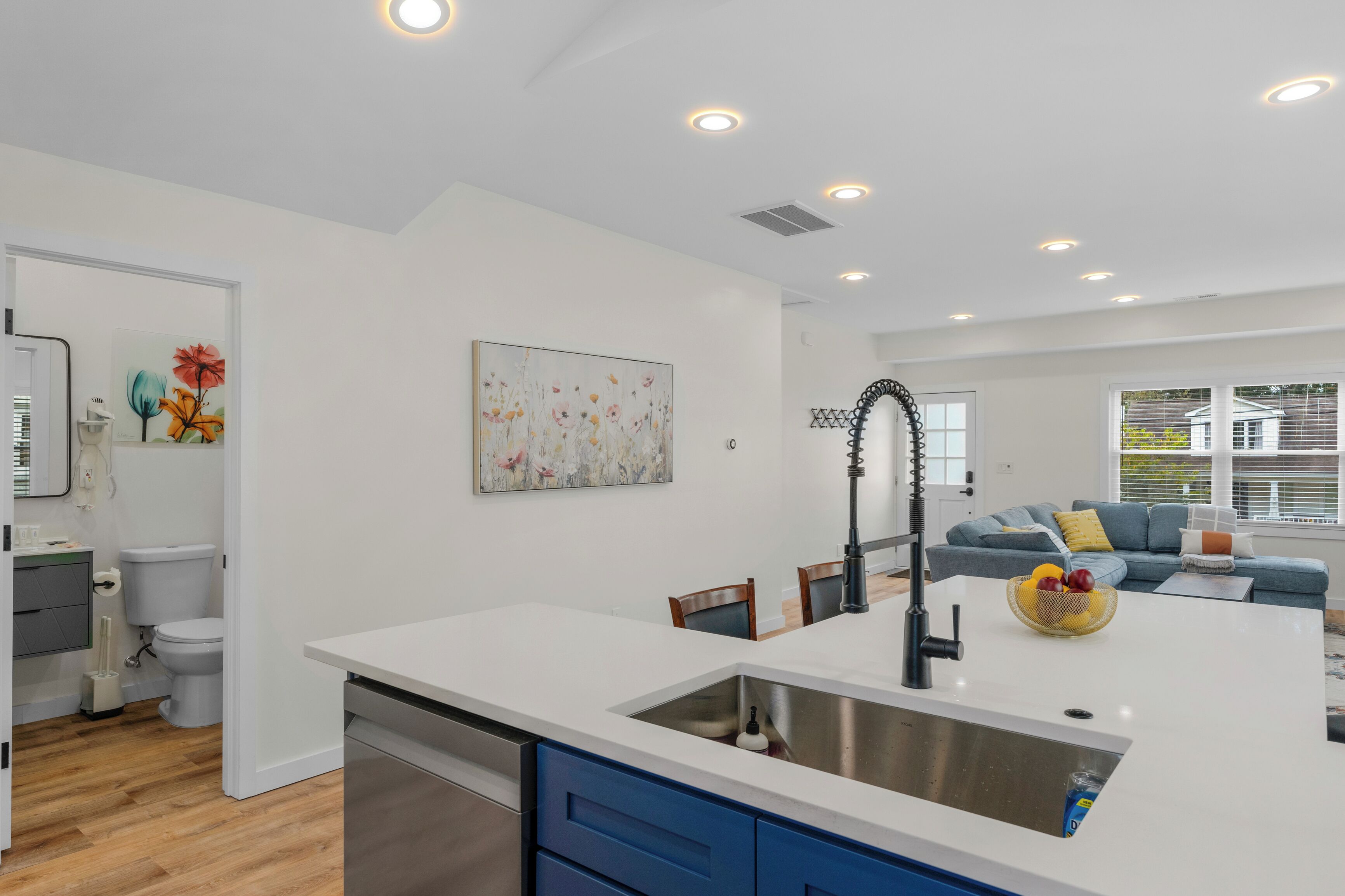 A modern kitchen with a central island, a dining area with chairs, a sofa, and a large window.