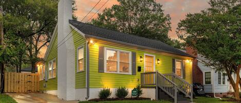 A two-story house with a green exterior, a front porch, and a visible front yard.