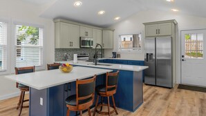 A modern kitchen with a central island, blue cabinets, stainless steel appliances, and a white door.