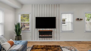 A living room with a flat-screen TV mounted on the wall, a sofa, a coffee table, and a fireplace.