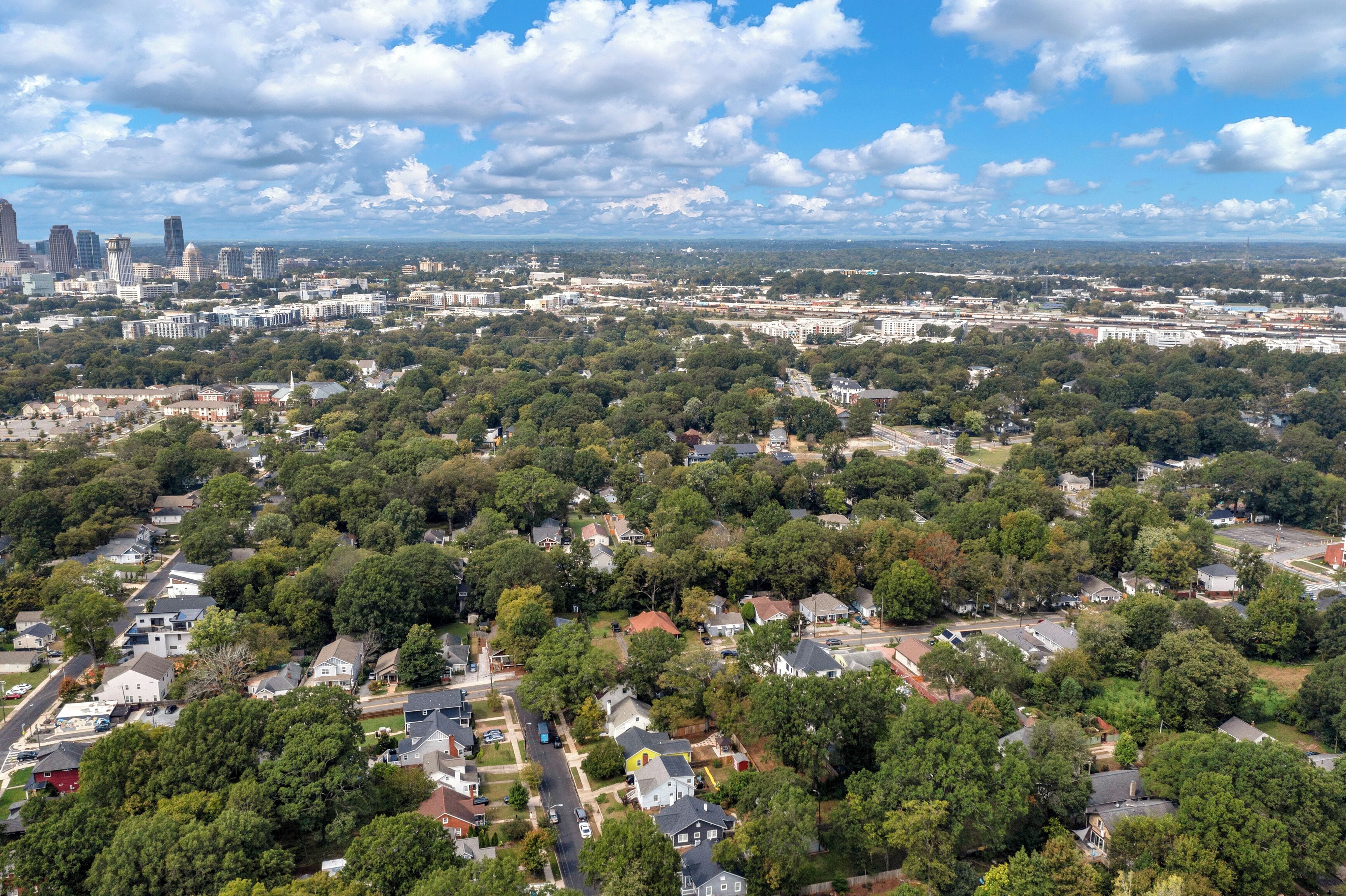 An aerial view of a residential area with houses, trees, and a distant city skyline.