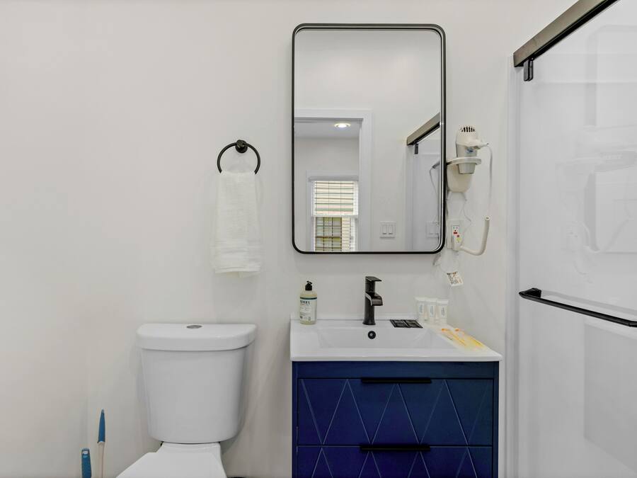 A modern bathroom with a white toilet, a sink with a mirror above it, and a blue cabinet.