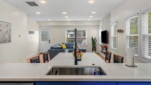A modern kitchen with a central island, a dining area with a sofa, and a TV mounted on the wall.