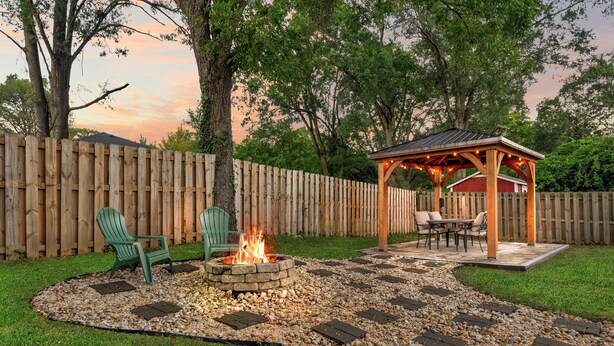 A backyard with a fire pit, outdoor seating, and a wooden gazebo.