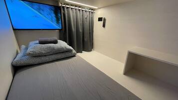 A modern bedroom with a bed, a TV mounted on the wall, a remote control, and a small shelf.