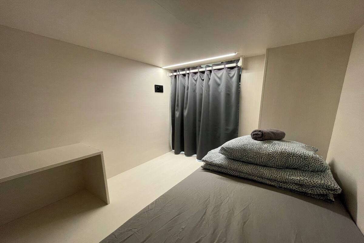 Un dormitorio pequeño y minimalista con una cama individual, una mesita de noche y una cortina.