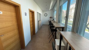 A hallway with wooden doors, a long table with chairs, and large windows offering a view of the outside. - Sleep&Go Hostel (Ljubljana)
