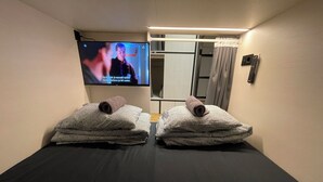A room with two massage tables, each with a towel and a remote control. A television is mounted on the wall, displaying a program. - Sleep&Go Hostel (Ljubljana)