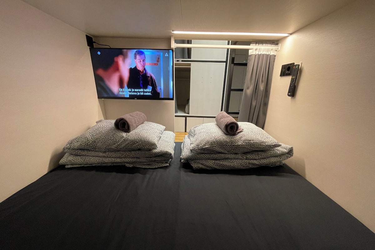 Una habitación con dos camillas de masaje, cada una con una toalla y un control remoto. Un televisor está montado en la pared, mostrando un programa.