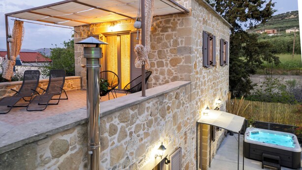 Une maison en pierre dotée d’un patio, d’un espace salon extérieur et d’un jacuzzi.