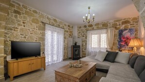 Un salon avec des murs en pierre, un meuble TV en bois, un canapé, une table basse et une lampe.