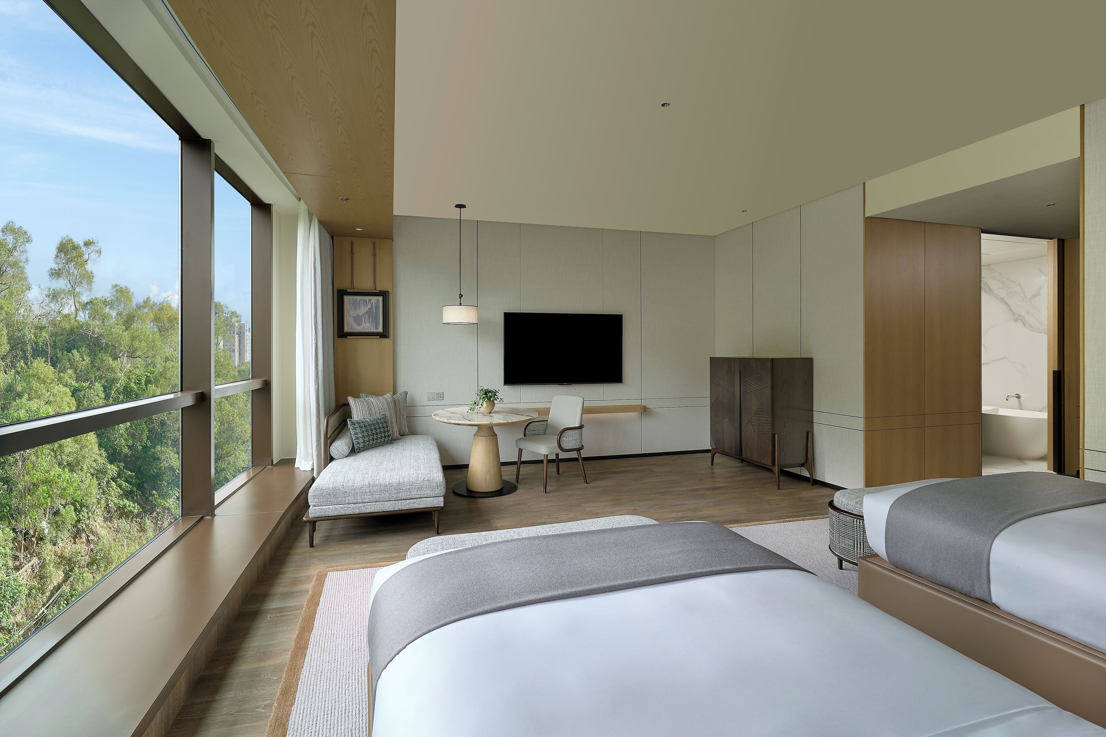 Een moderne hotelkamer met grote ramen, een flatscreen-tv, een ronde eettafel en een bank.