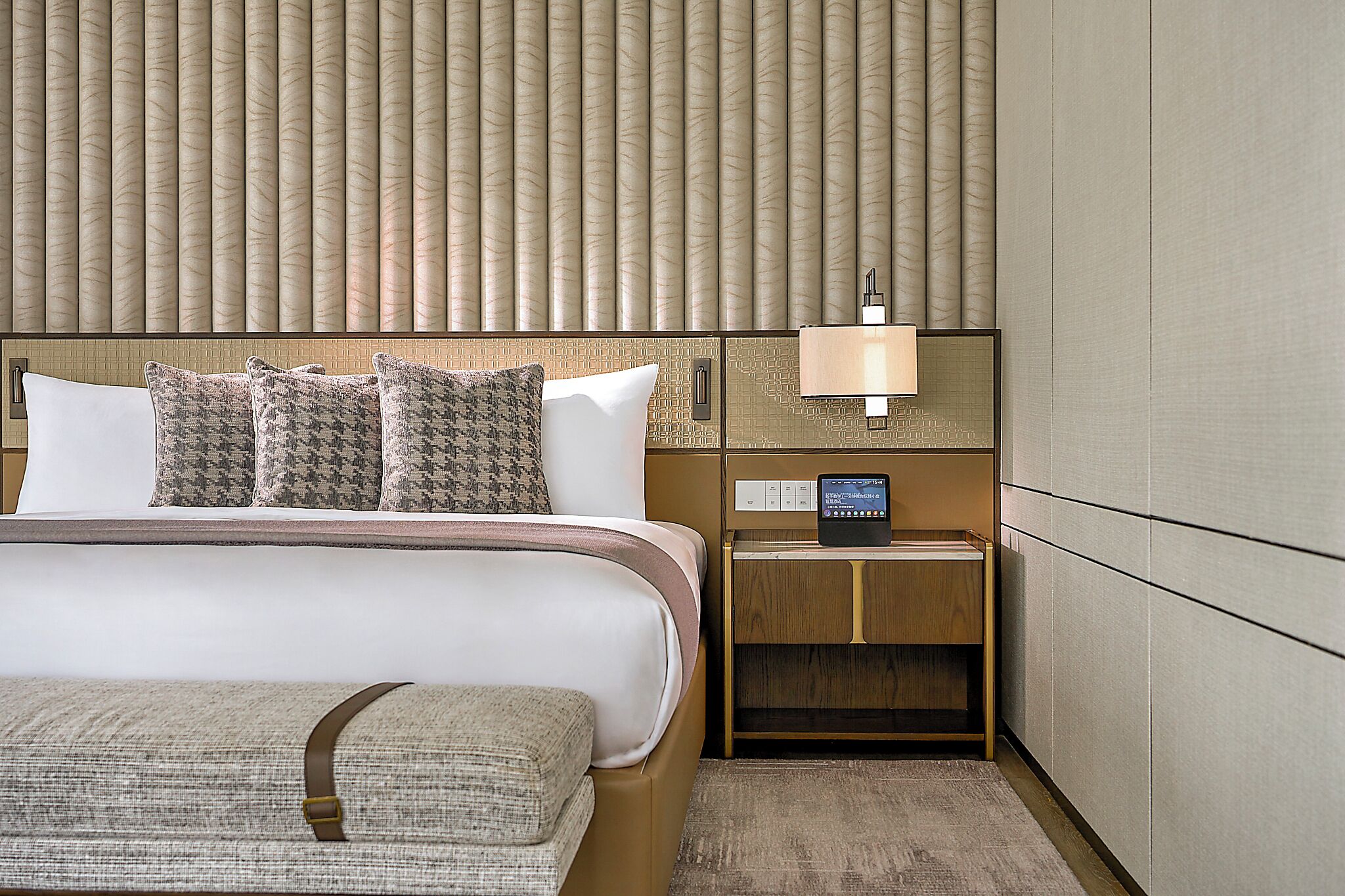 Une chambre d’hôtel équipée d’un lit, d’une table de chevet, d’une lampe et d’un panneau de commande.