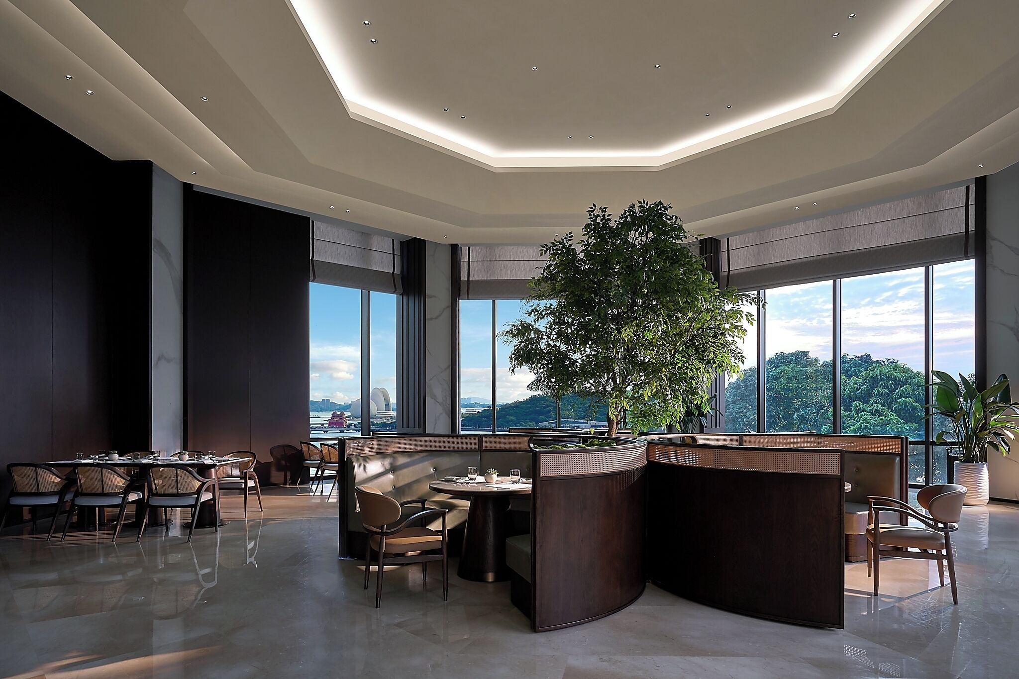 Un interior moderno con un gran árbol, zonas de estar y ventanas amplias que ofrecen vistas.