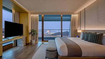 A modern hotel room with a large bed, a flat-screen TV, a view of the cityscape, and a balcony.