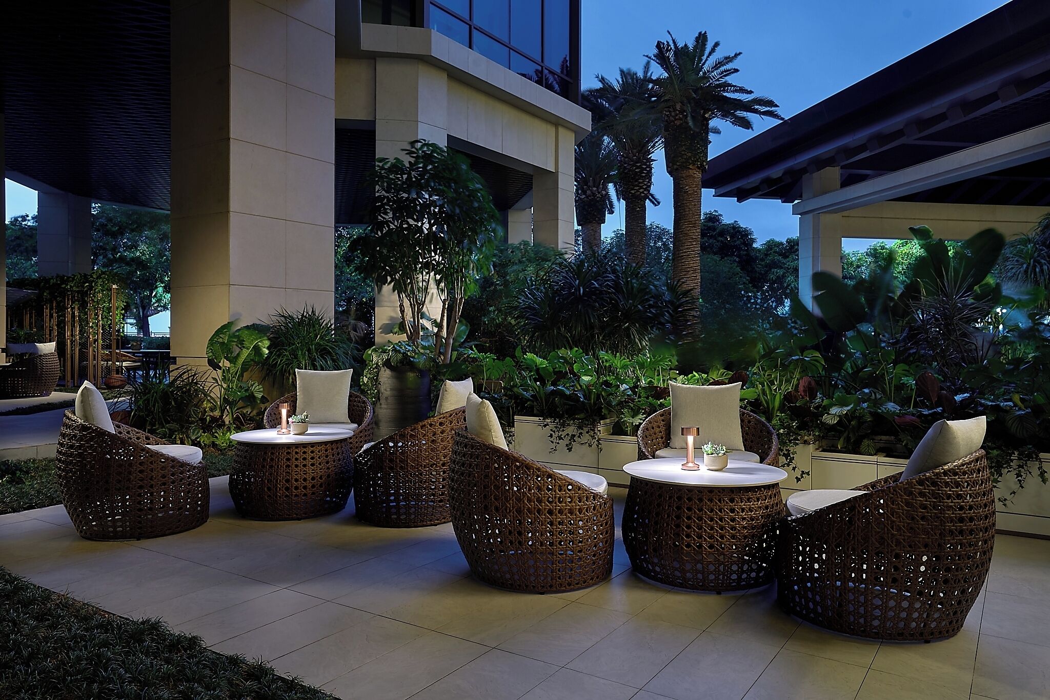 Outdoor wicker furniture with cushions, a round table, and a potted plant.