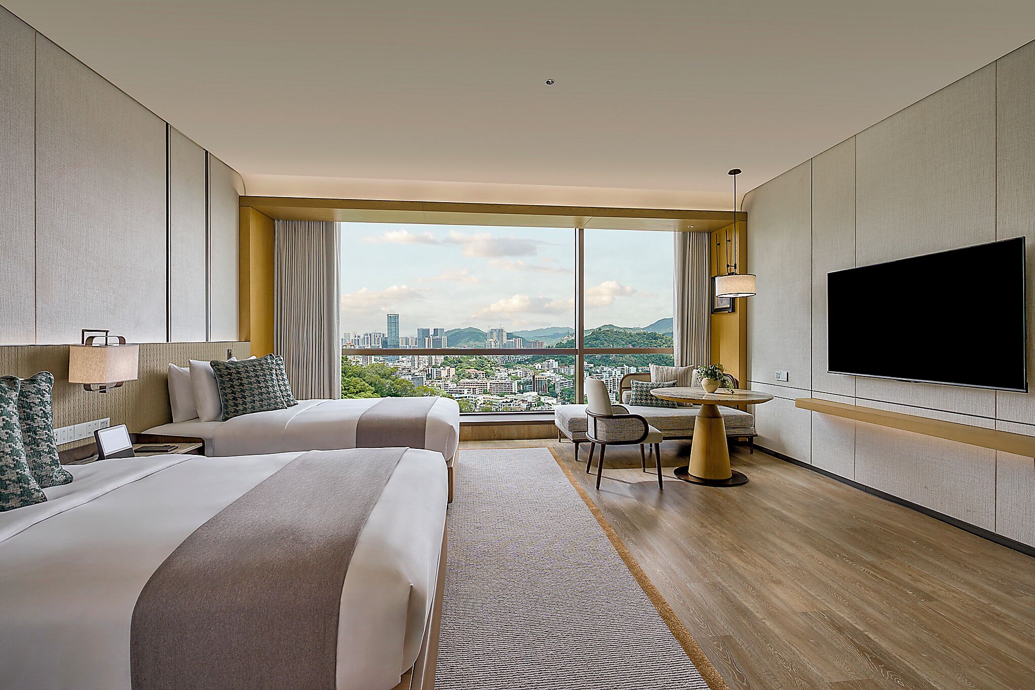 A hotel room with two beds, a dining table, a TV, and a city view.