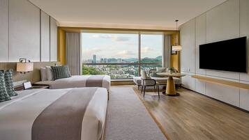 A hotel room with two beds, a dining table, a TV, and a city view.