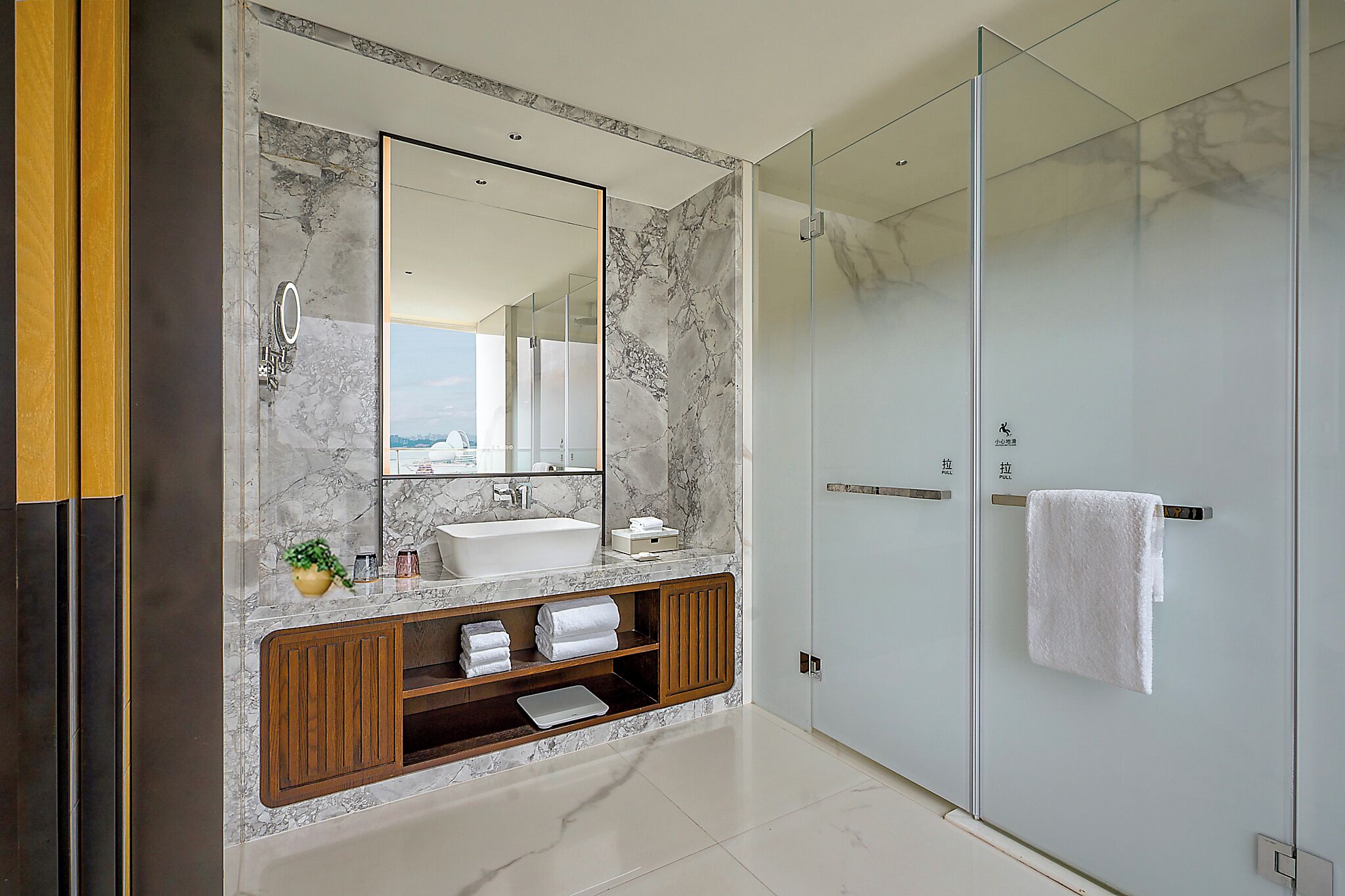Une salle de bain moderne avec un meuble-lavabo en marbre, un grand miroir, une douche en verre et un porte-serviettes.