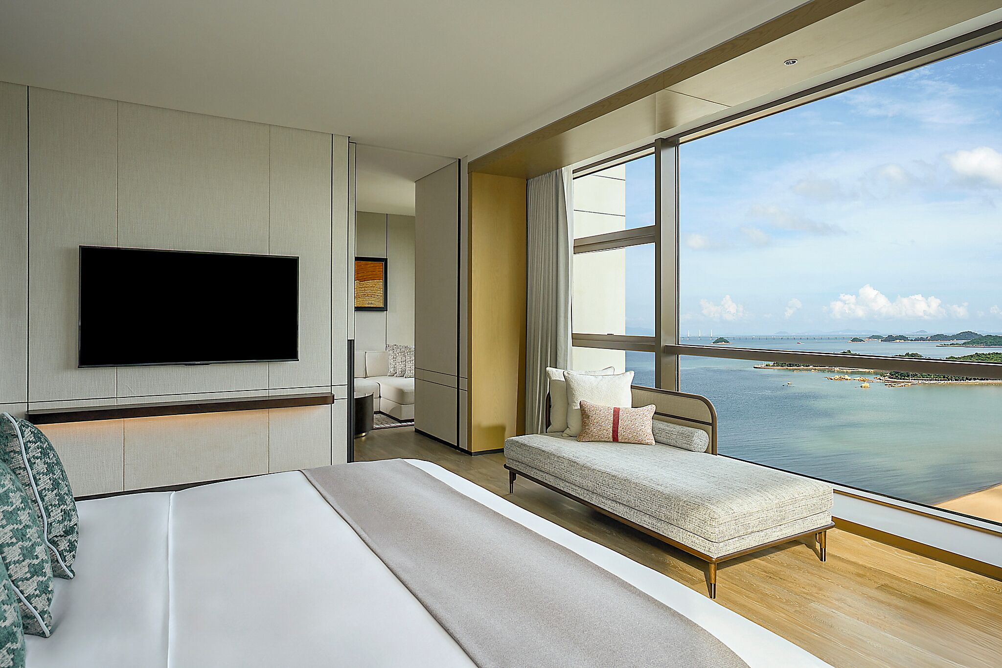 Een moderne hotelkamer met een groot bed, een televisie, een bank en uitzicht op zee.