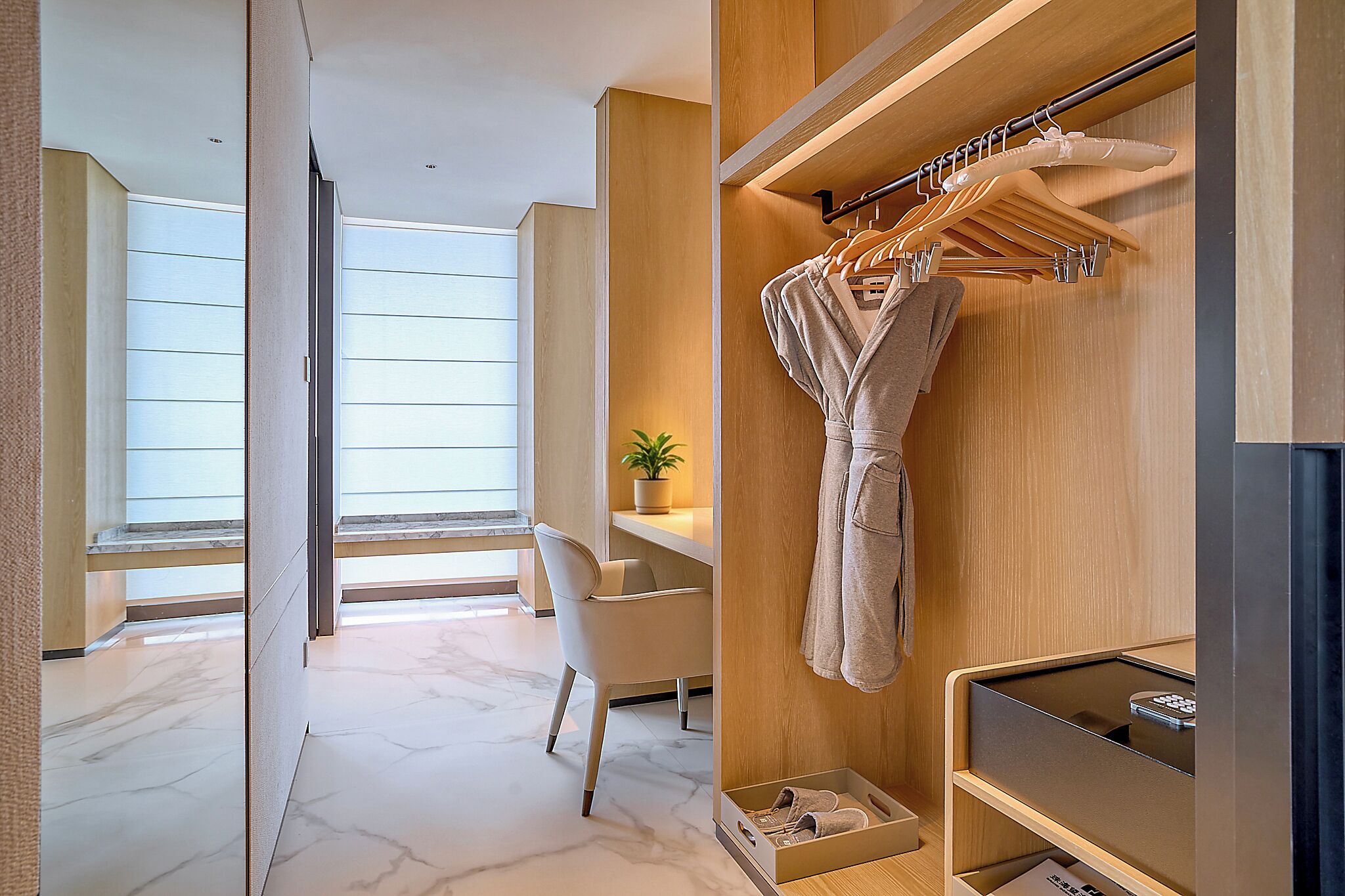 A modern bathroom with a wooden vanity, a robe hanging on a rack, and a potted plant on the shelf.