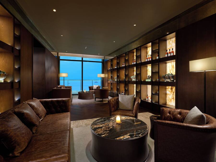 Een moderne lounge met leren banken, een marmeren salontafel en een boekenkast met flessen.