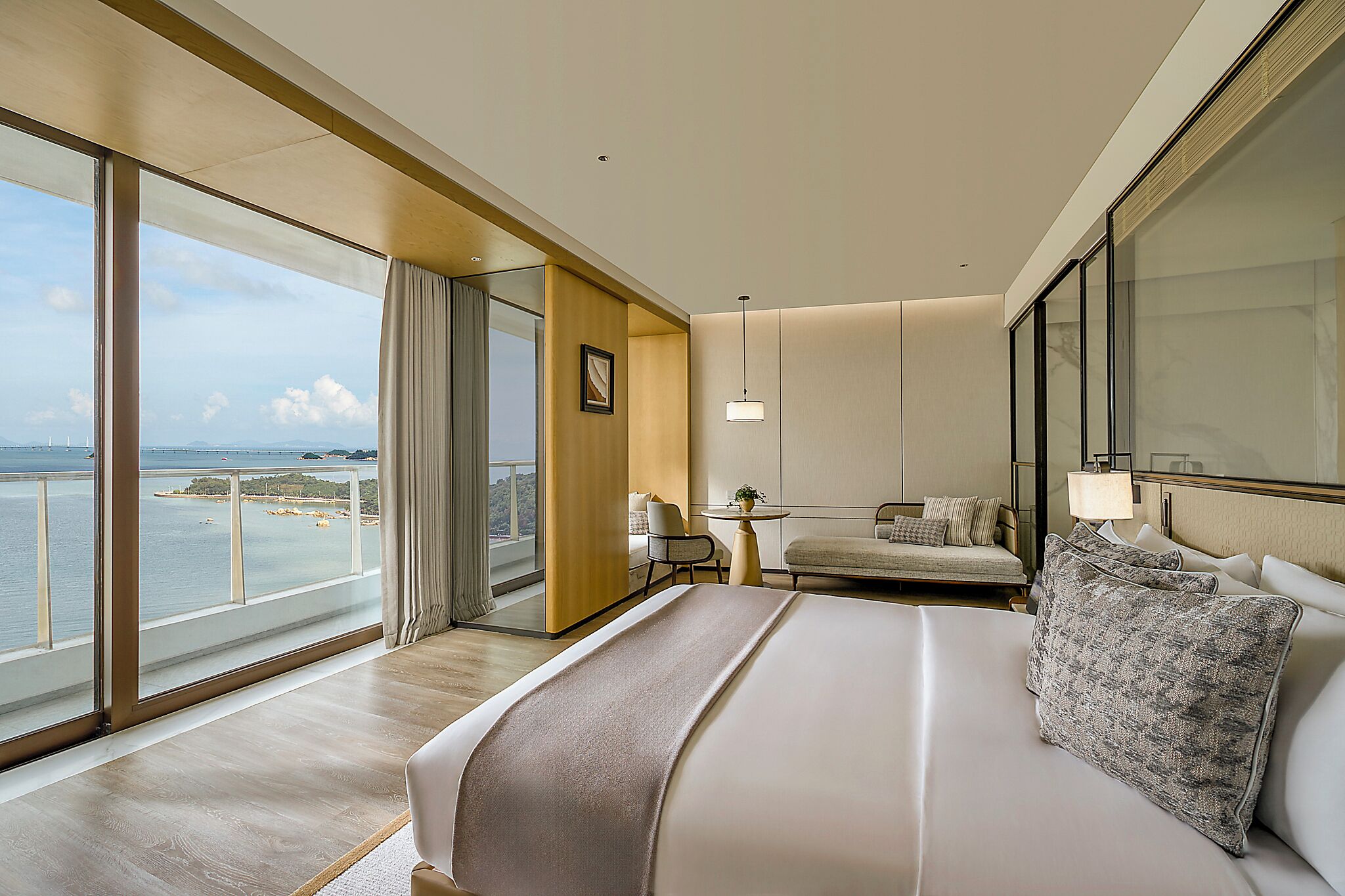 Ett modernt hotellrum med en stor säng, en sittgrupp och en balkong med utsikt över havet.