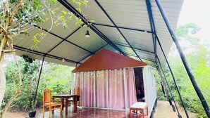 Un área de estar al aire libre techada, con mesa y sillas de madera, rodeada de abundante vegetación.