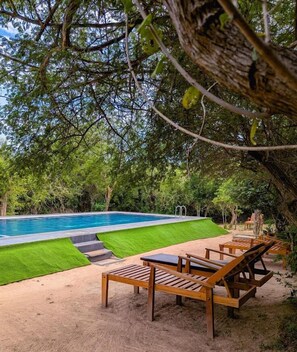 A swimming pool with a sandy deck, surrounded by lush greenery and wooden lounge chairs. - Lowin Yala (Yala)