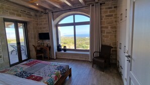 Une chambre avec un grand lit, un bureau, une chaise et un téléviseur. Il y a une fenêtre qui offre une vue sur le paysage.