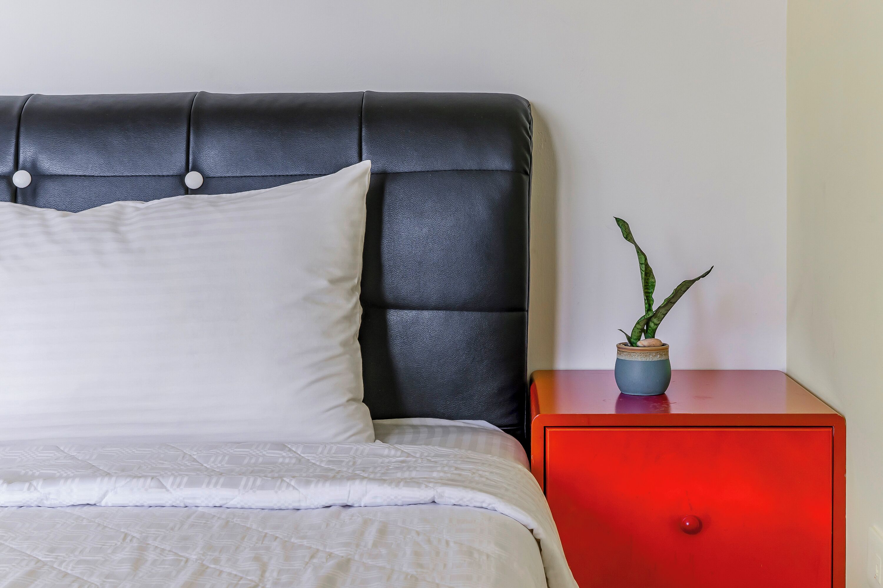 Un lit bien fait, avec une couette blanche et une tête de lit noire, recouverte de tissu et ornée de boutons.