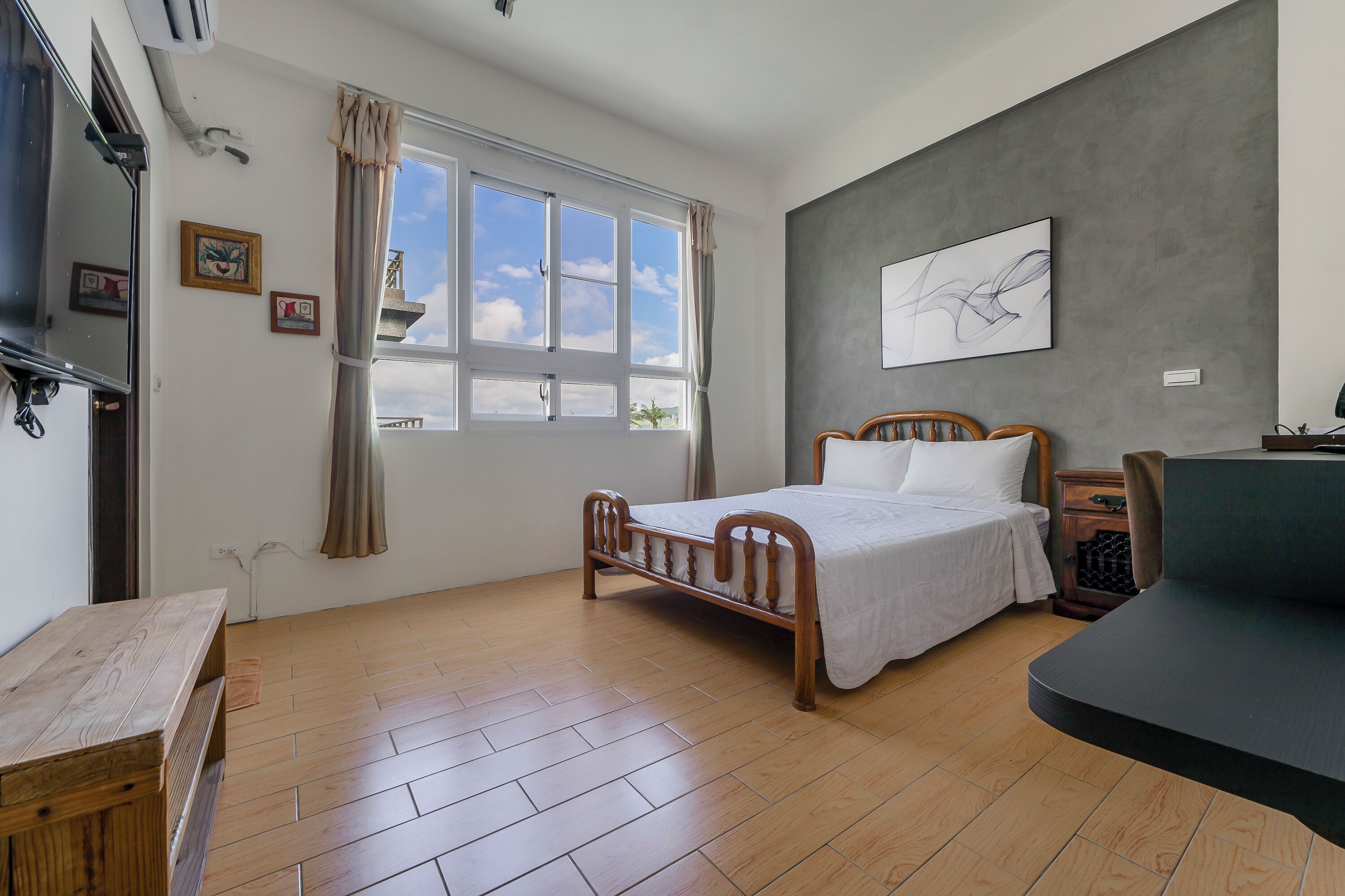 A bedroom with a wooden bed, a window with curtains, a grey accent wall, and a wooden bench.