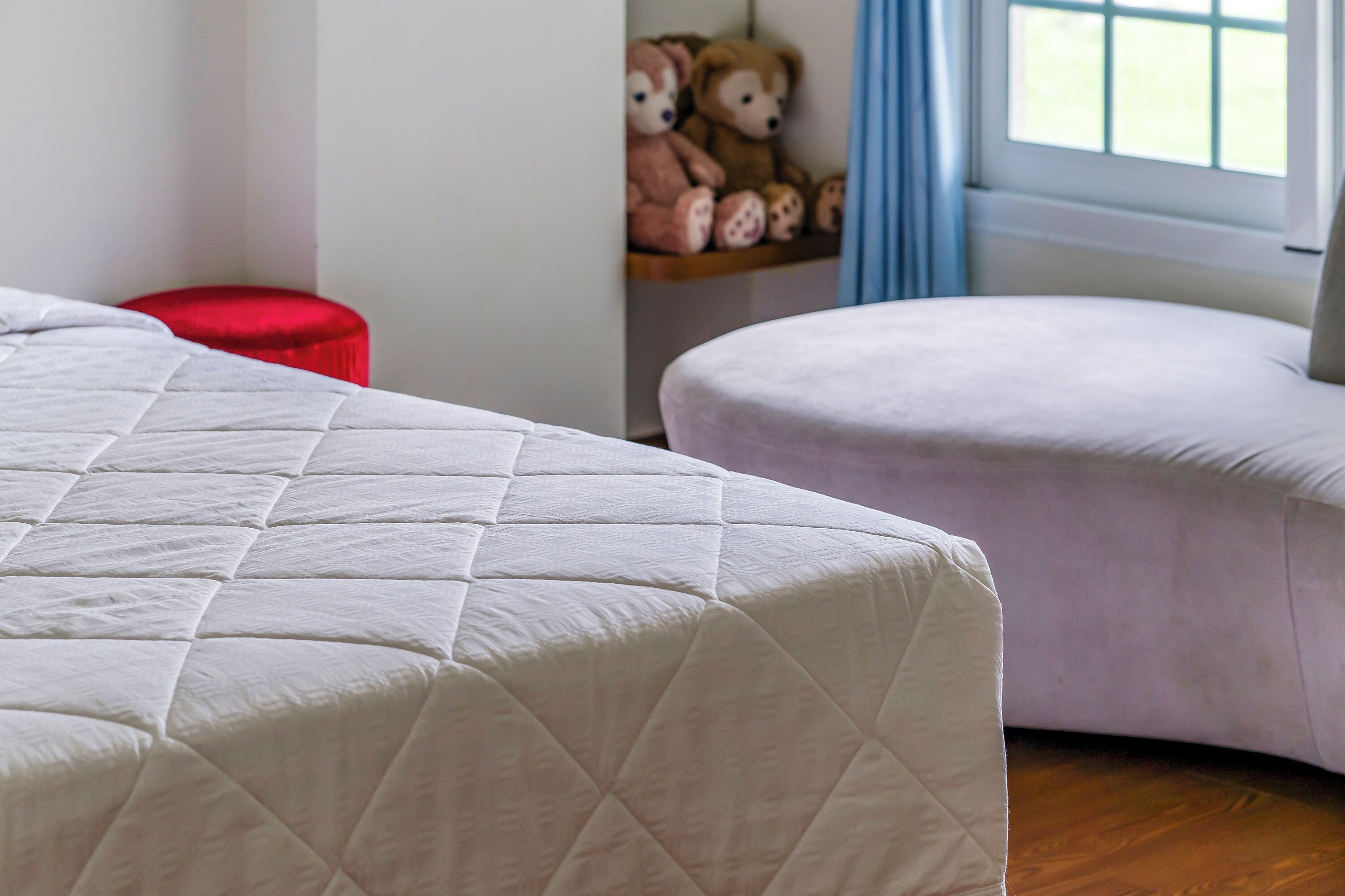 A bedroom with a large bed, a red ottoman, and a window with daylight.