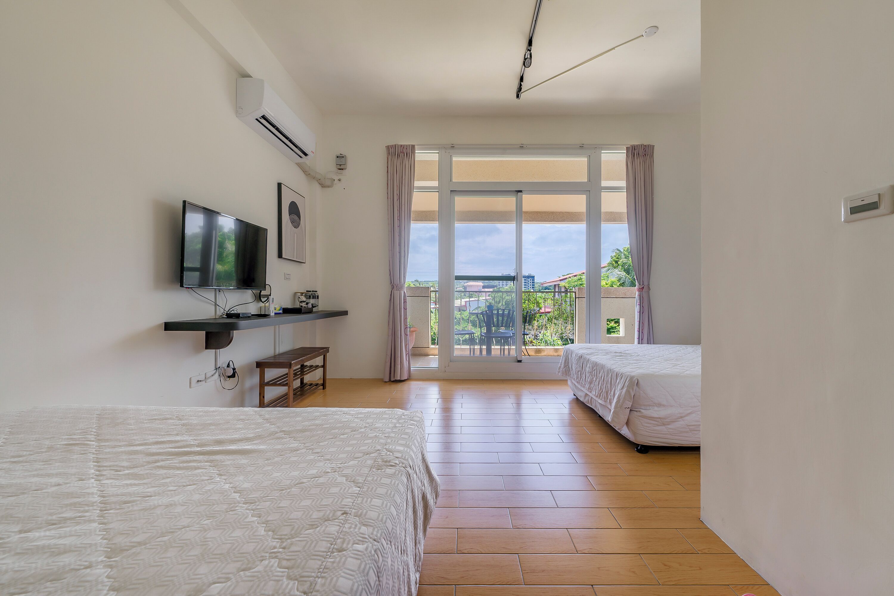 A hotel room with two beds, a TV, an air conditioner, and a balcony with a view.
