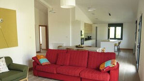 A spacious living area with a red sofa, a green armchair, and a wooden coffee table. A kitchen is visible in the background. - Sagarmintxe. Tourist apartment. (Berriatua)