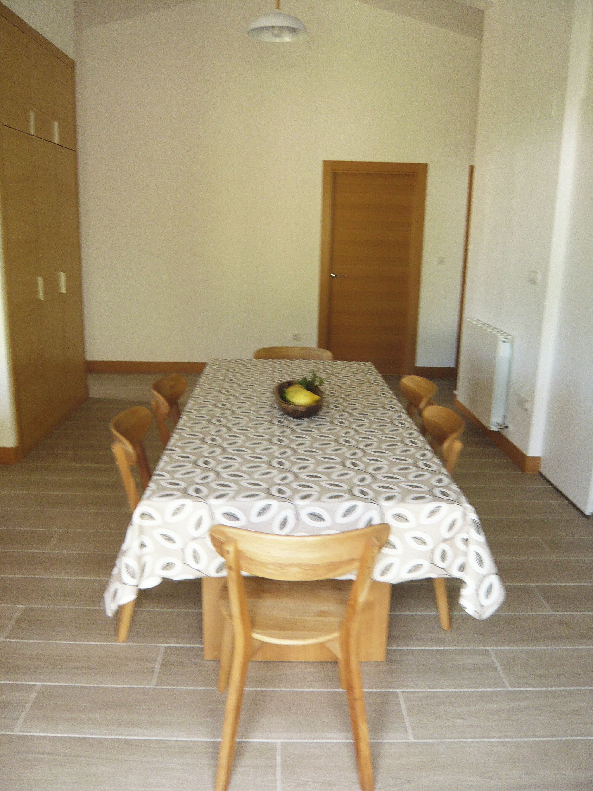 A dining area with a table covered by a patterned tablecloth, surrounded by wooden chairs.