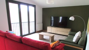 A living room with a red sofa, a green sofa, a wooden coffee table, a TV on a wooden cabinet, and a floor lamp. - Sagarmintxe. Tourist apartment. (Berriatua)