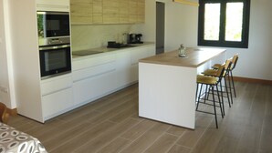 A modern kitchen with white cabinetry, a built-in oven, a coffee maker, and a bar area with stools.