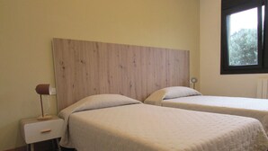 A room with two beds, a wooden headboard, a bedside table with a lamp, and a window with a view of trees. - Sagarmintxe. Tourist apartment. (Berriatua)