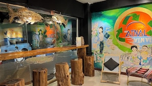 Un espace d’accueil doté d’une cloison en verre, de tabourets en bois, d’un comptoir de réception et d’une fresque colorée représentant une scène de famille.