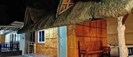 A thatched-roof structure with a wooden bench and a table outside.