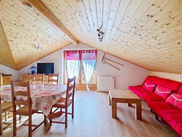A cozy attic room with a wooden ceiling, a dining table with chairs, a red sofa, and a window with curtains. - BALCONS DE CHATEL BC19 NATURE & MOUNTAIN (Châtel)