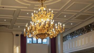 A hotel lobby with a large chandelier, a central table with a vase of flowers, and multiple seating areas.