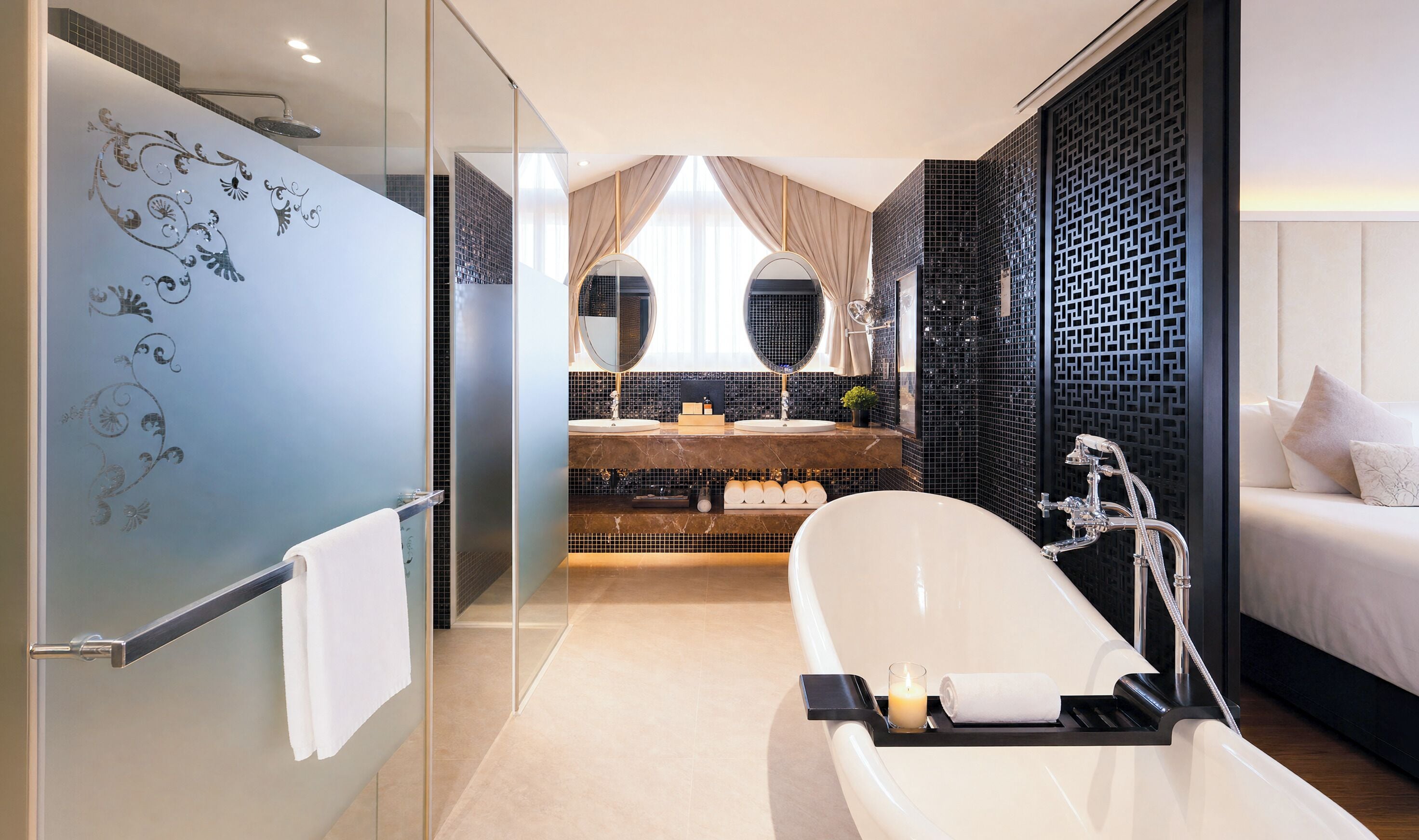 A modern bathroom with a glass shower, a bathtub, a double sink vanity, and a bed with a decorative headboard.