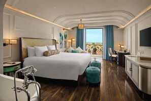 A spacious hotel room with a large bed, a sitting area with a view, a bathtub, and a TV.