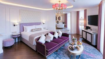 Ein modernes Hotelzimmer mit einem großen Bett, einer Couch, einem runden Couchtisch, einem Fernseher und einem durchgehenden Türspalt sichtbaren Badezimmer.