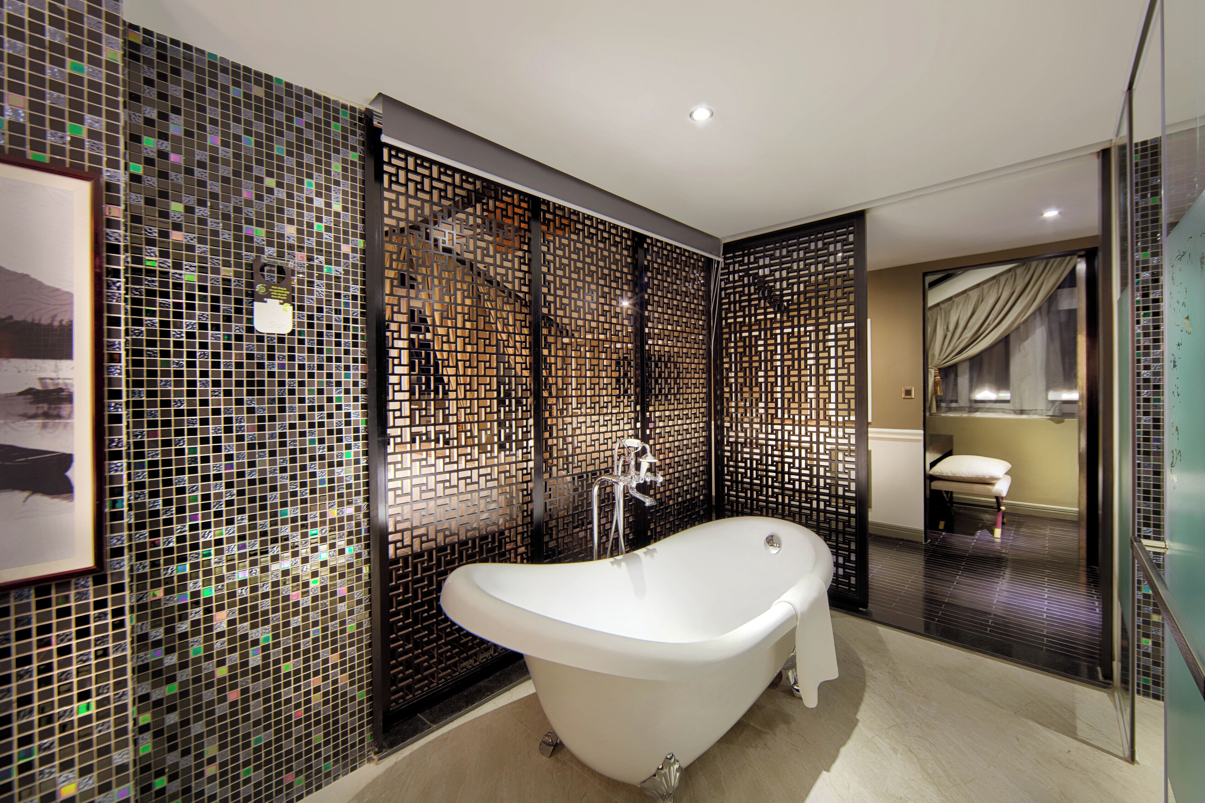 Une salle de bain moderne avec une baignoire sur pieds, des murs recouverts de mosaïques et une cloison en verre.