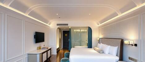 A hotel room with a large bed, a desk, a TV, and a bathroom visible through an archway.