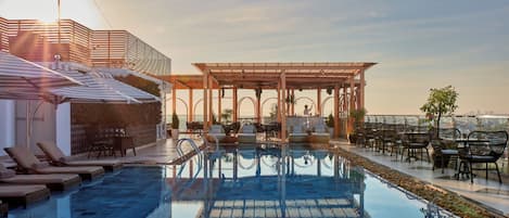 A rooftop pool area with lounge chairs and a pergola.