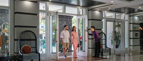 A modern lobby with a glass door entrance, a black chair, and a potted plant.